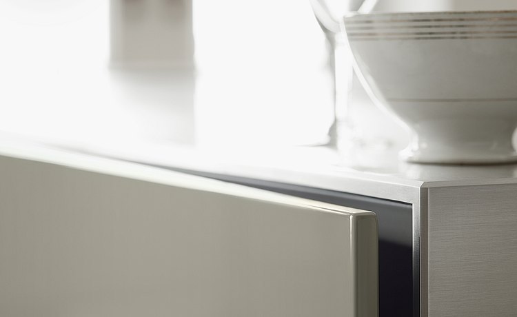 Close-up: combination of a brushed stainless steel surface with light-gray lacquer front panels