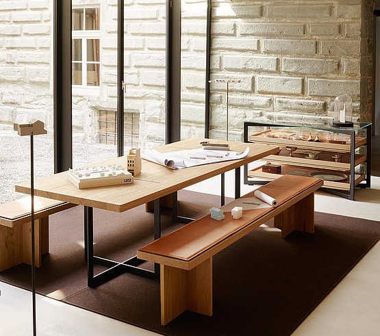 Aluminiumrahmen des Tisches harmoniert durch gleiches Designprinzip trotz Materialgegensatz mit gekreuzten Holzfüßen der Bank 