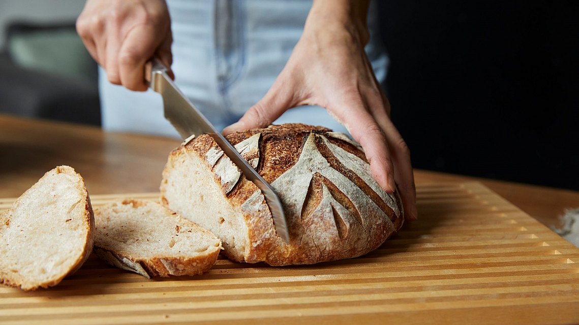 Frisches Brot wird auf einem bulthaup Brotschneidebrett aufgeschnitten.
