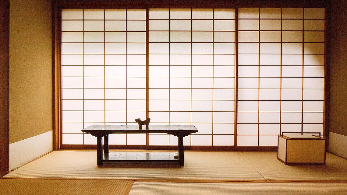 Schmuckecke mit zentralem Holztisch und kleiner Holzfigur. Im Hintergrund die geschlossene, mit Washi-Papier bezogene Blende.