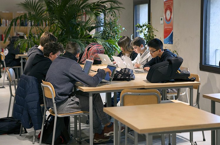 Eine Gruppe Jugendlicher arbeitet an einem Tisch an ihren Computern
