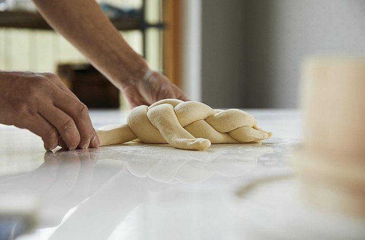 Brotteig wird zu einem kunstvollen Zopf geformt.