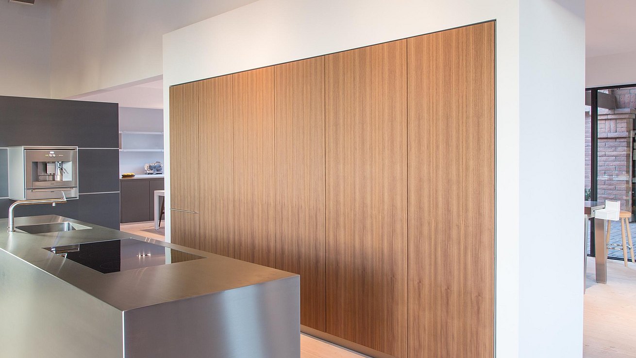 Detail of stainless steel monobloc with tall cabinets in walnut veneer.